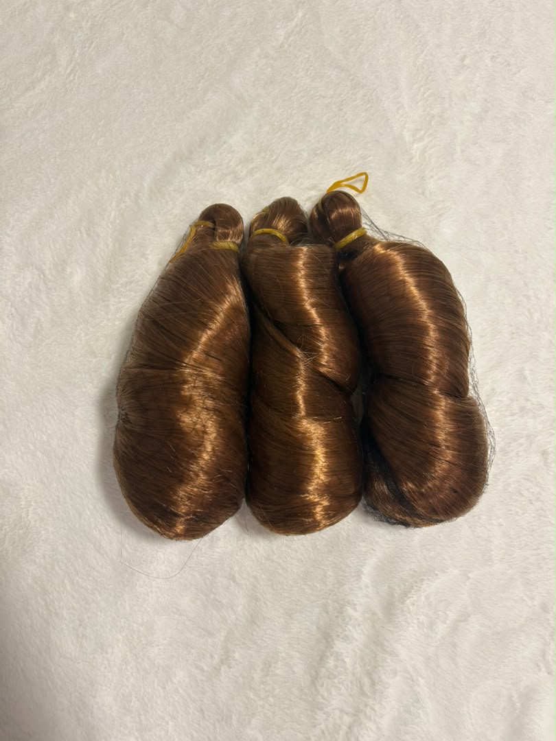 Three bundles of brown hair extensions on a textured beige surface